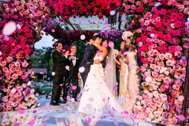 Couple at a ceremony framed by a wall of pink and red roses, Samuel Lippke Studios