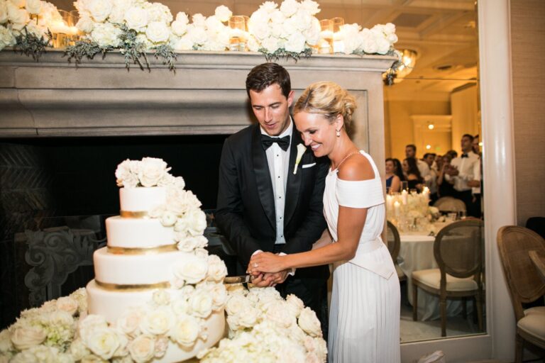 Couple cutting a tall white cake beside a fireplace, Samuel Lippke Studios
