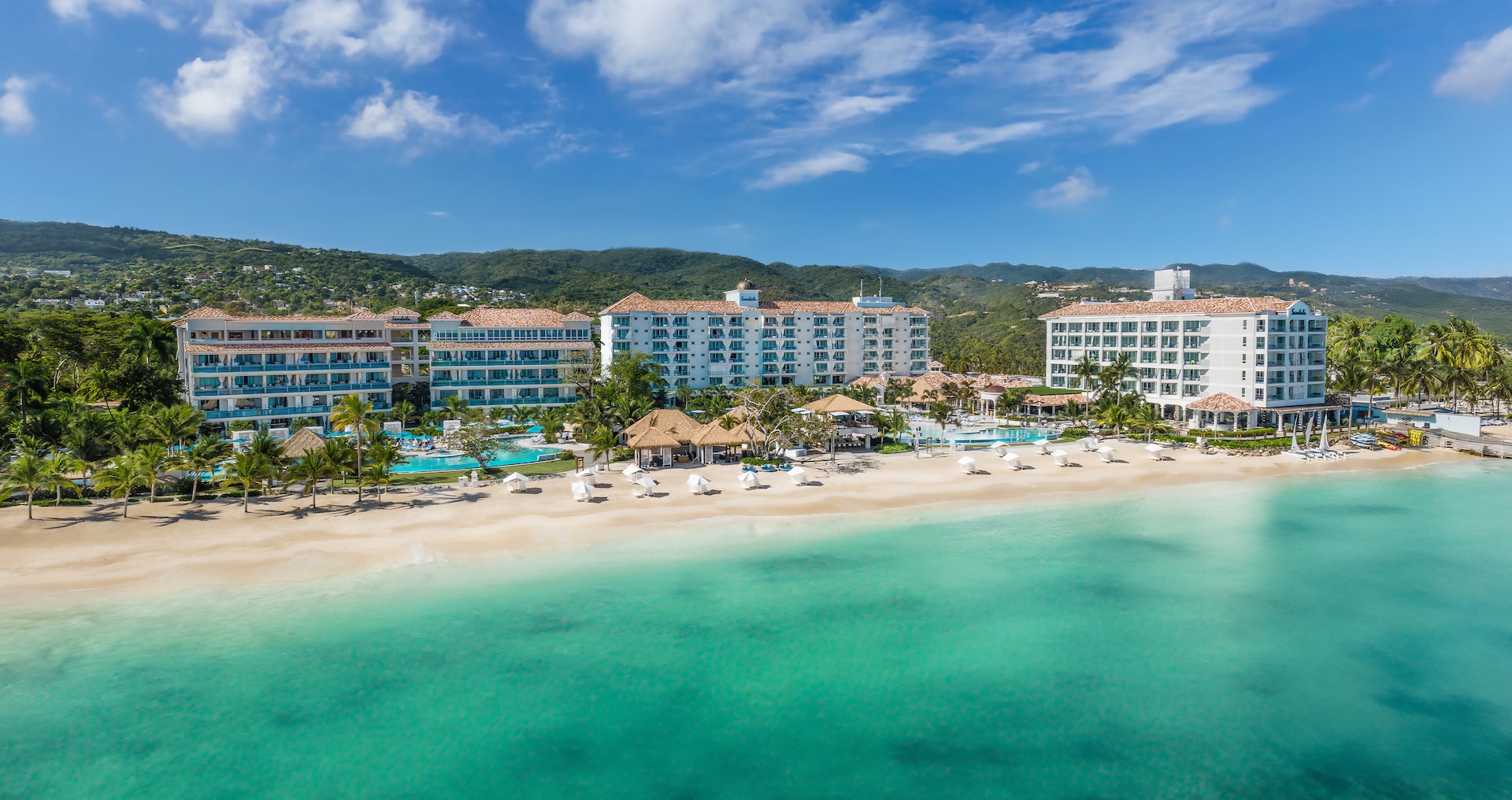 Aerial view of the resort buildings and pools set back from the beach, Sandals Dunn's River