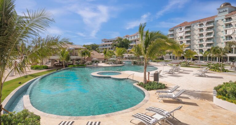 A pool with a whirlpool and loungers, with a resort tower behind, Sandals Dunn's River