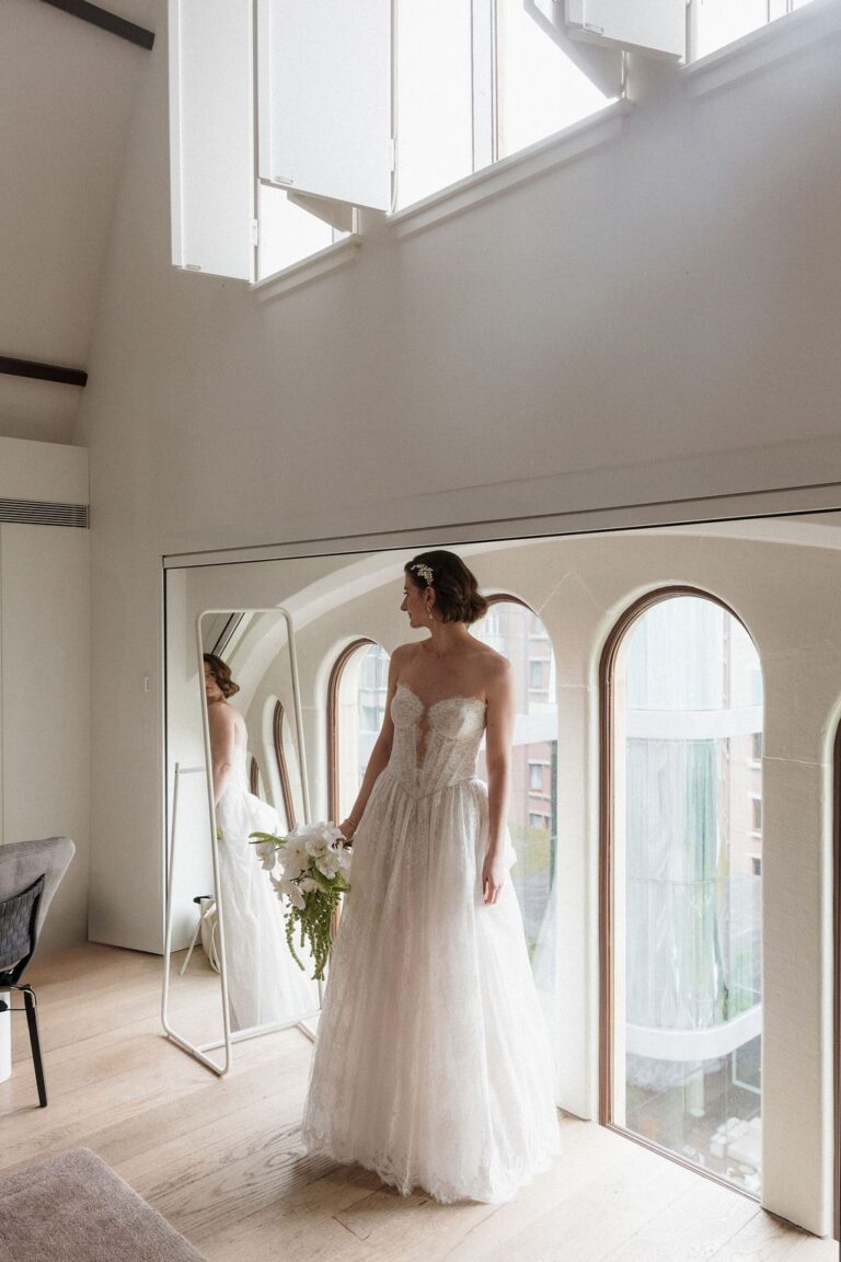 Bride in a lace gown beside an arched window and mirror, Amsterdam, Sante Weddings