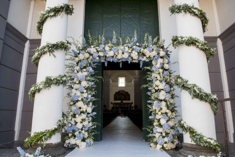 Church doorway framed with blue and white flowers and greenery garlands, Sara D'Angelo