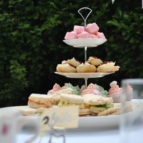 A tiered afternoon tea stand with sandwiches and cakes in a garden