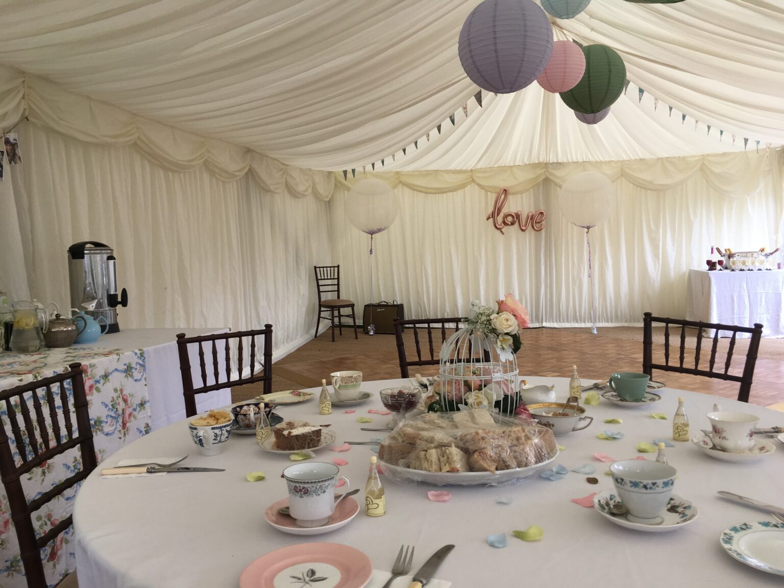 A marquee set for a tea party reception with paper lanterns and vintage china