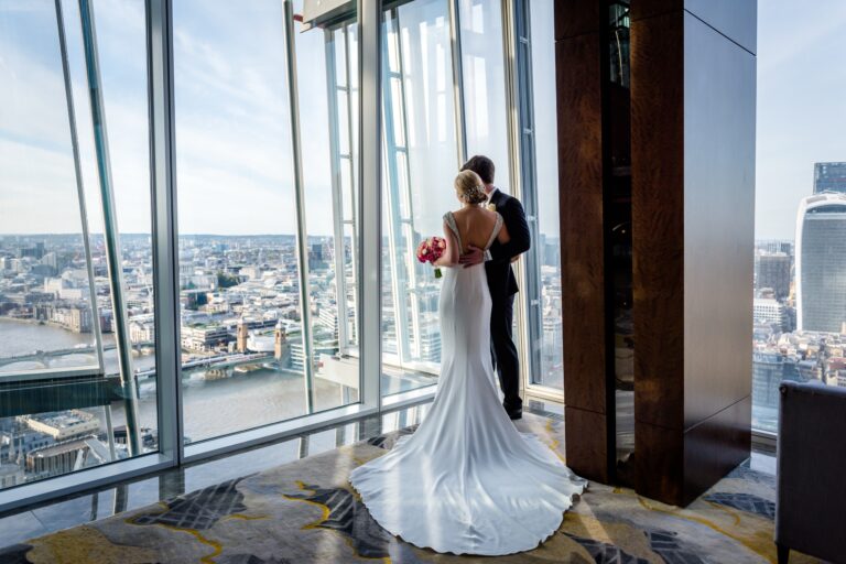 A bride and groom at the window above the river and the City, her train spread across the carpet, Shangri-La Hotel, The Shard, London