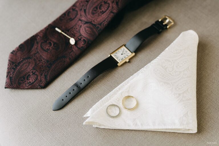 A burgundy paisley tie, a gold watch and two rings on white linen, Sicilian Wedding Day