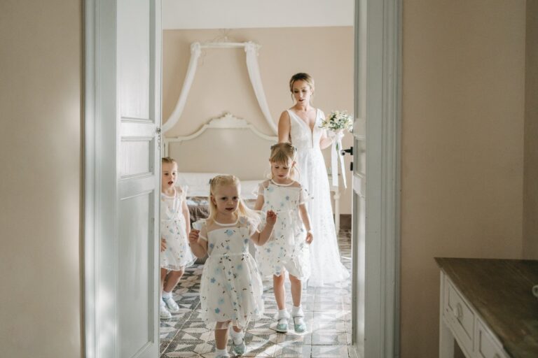 Three small girls running out through a white doorway, the bride behind them, Sicilian Wedding Day