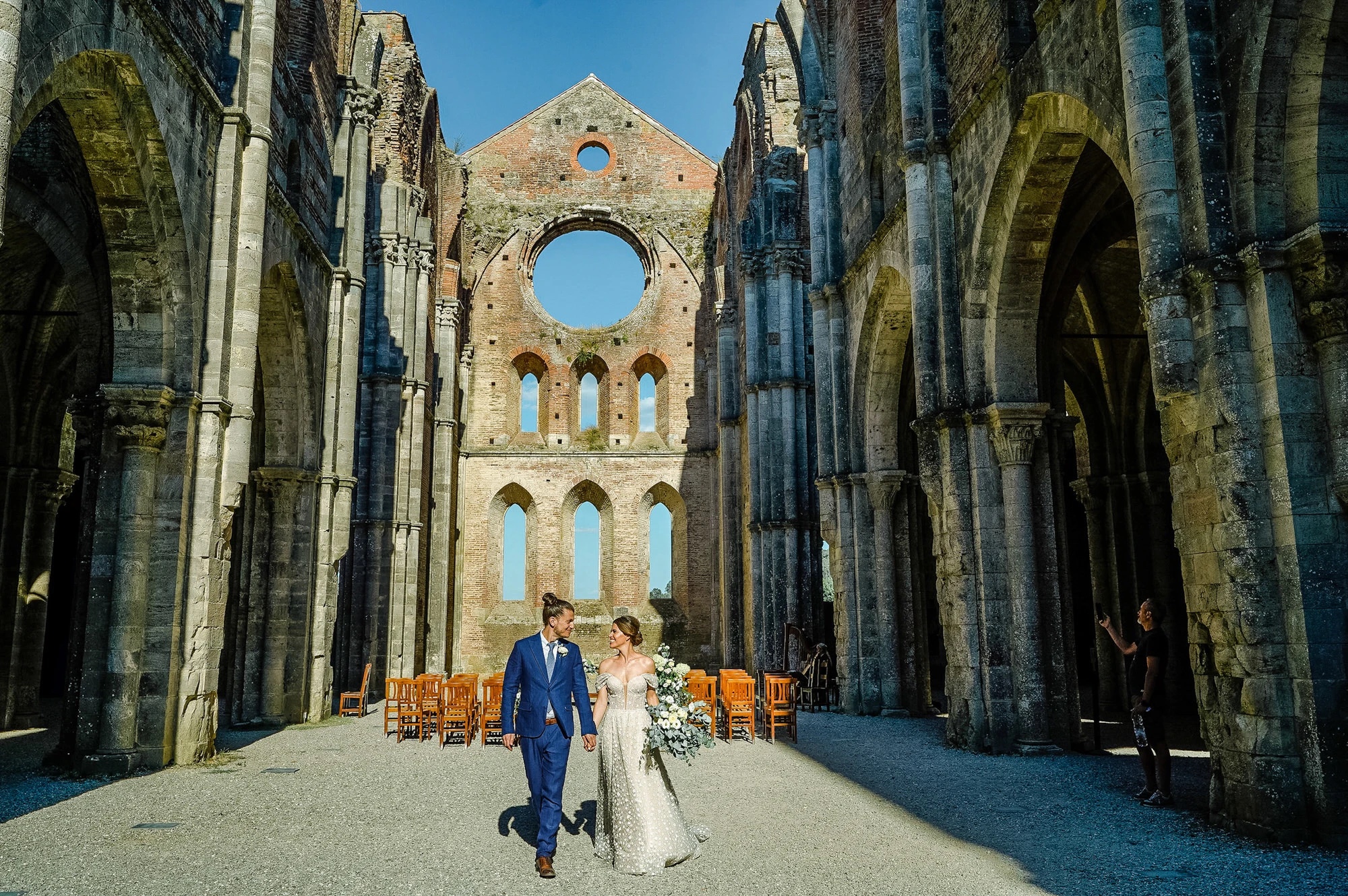Just married, walking out through the roofless nave of the Abbey of San Galgano after a civil ceremony, Simone Perini Photography