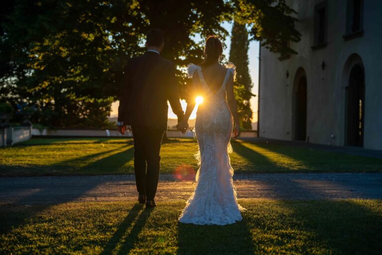 The couple walk across a villa lawn into the low sun, Simone Perini Photography
