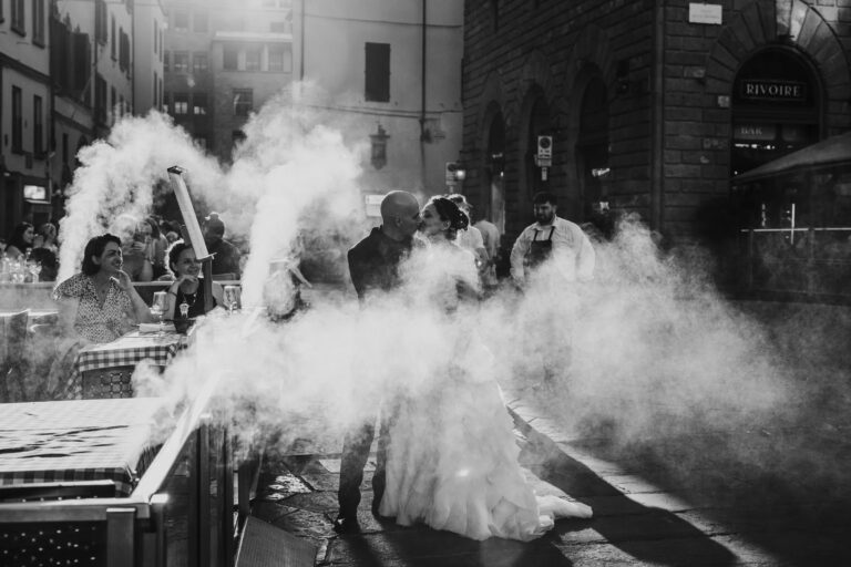 A kiss through drifting smoke beside cafe tables in central Florence, in black and white, Simone Perini Photography
