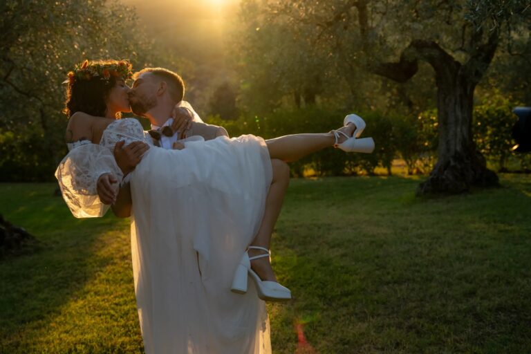 The groom carries his bride through an olive grove at golden hour, Simone Perini Photography