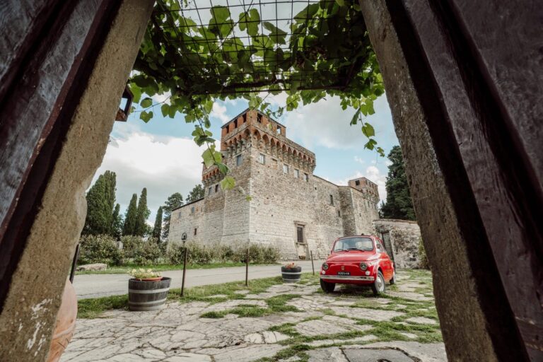 Castello del Trebbio framed through a vine pergola, a red Fiat 500 waiting in the courtyard, Simone Perini Photography