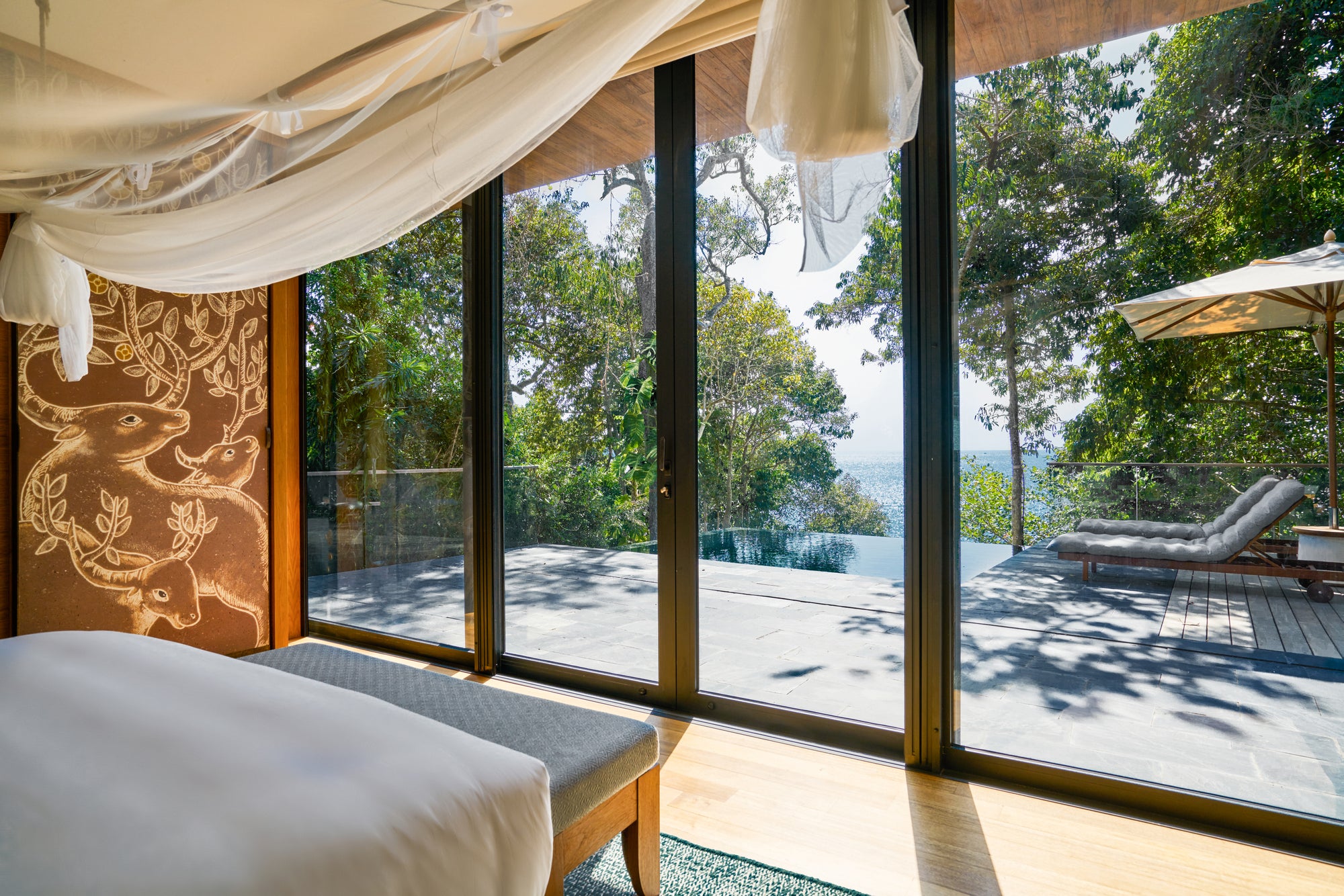 The bedroom of an Ocean Pool Villa Suite, opening onto its pool deck, Six Senses Krabey Island