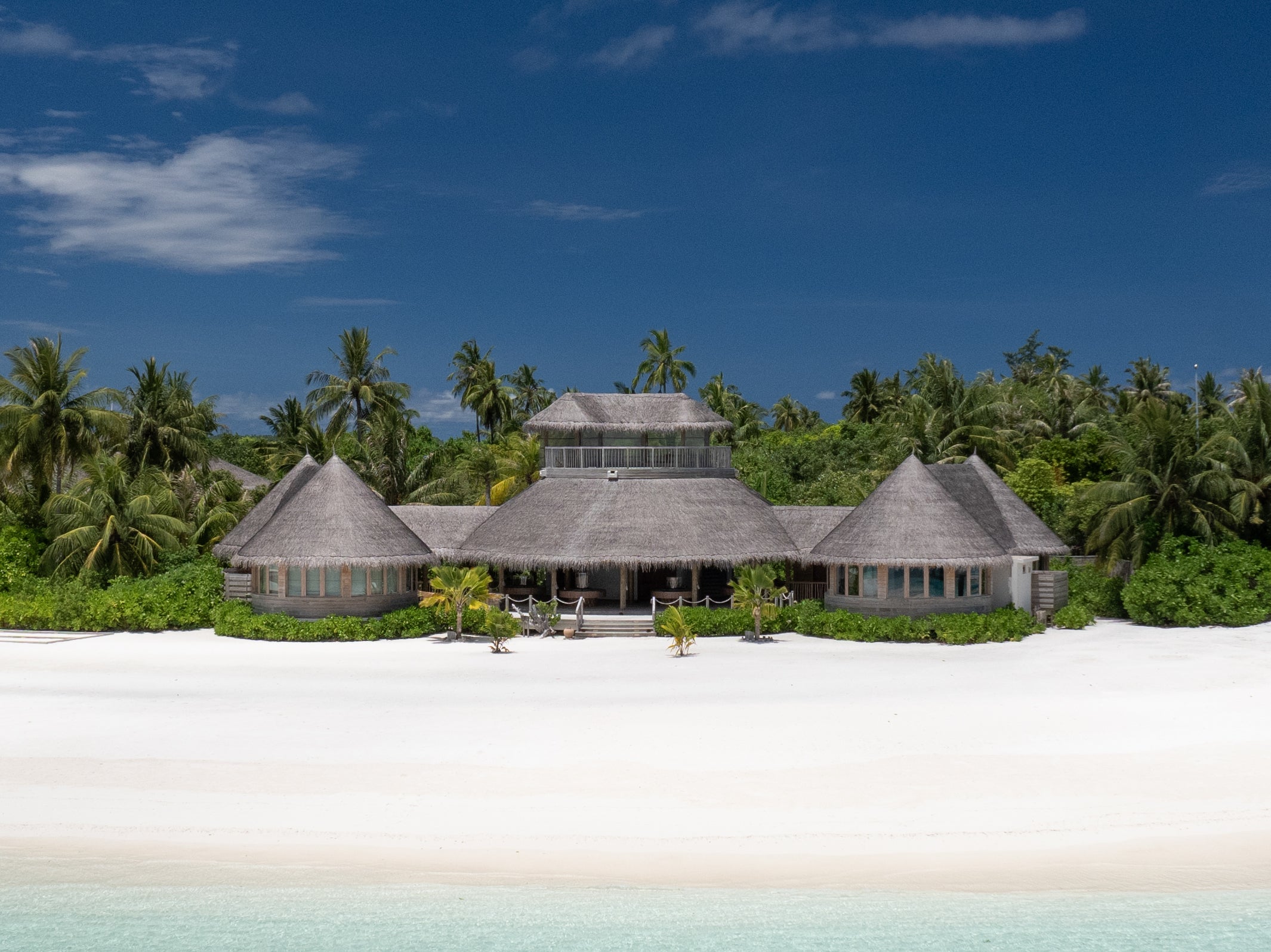 Thatched resort buildings behind a white sand beach, Six Senses Laamu