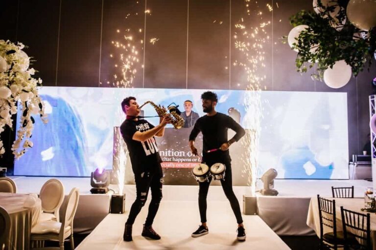 A saxophonist and a percussionist perform together on a spark-lit stage at a luxury wedding reception, Six15 Events