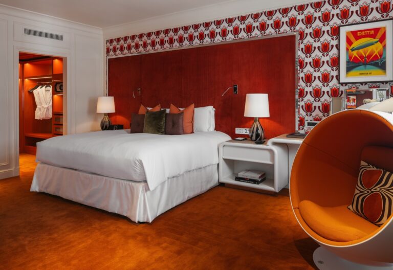 Suite 70 bedroom, with a 1970s-style egg chair, patterned wallpaper and a walk-in dressing area, Sofitel London St James