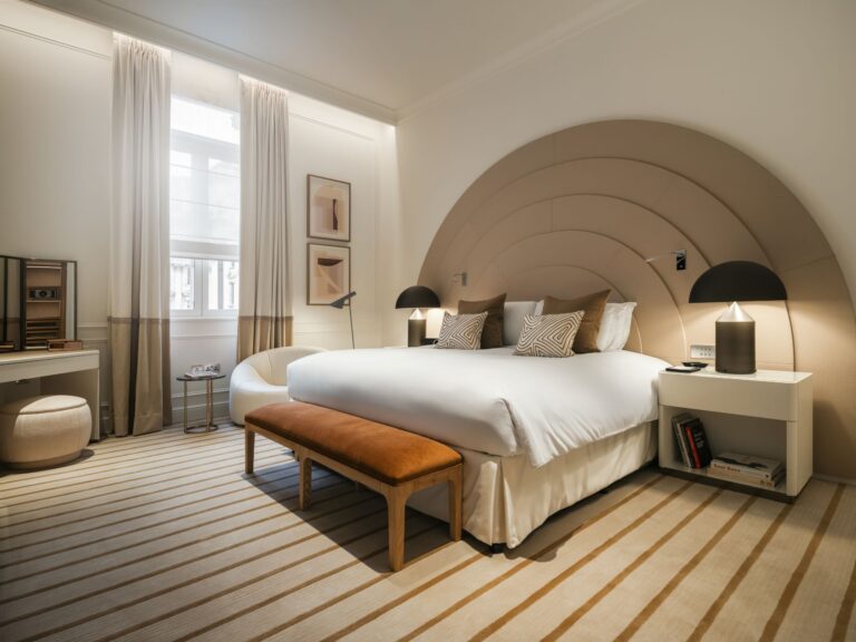 The Opera Suite bedroom with a curved, tiered headboard and striped carpet, Sofitel London St James