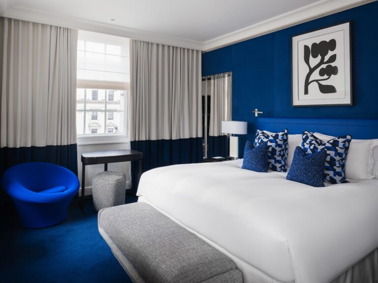 A Prestige Suite bedroom in deep blue, with a Pierre Paulin mushroom chair by the window, Sofitel London St James