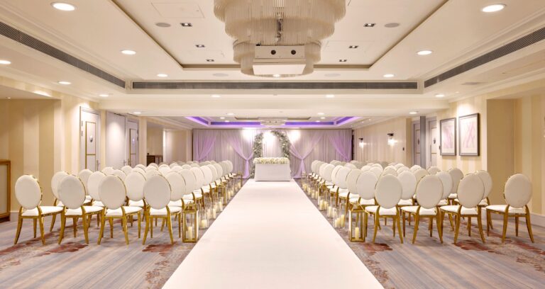 A ceremony layout with a long white aisle leading to a floral arch and lit drapes, Sofitel London St James