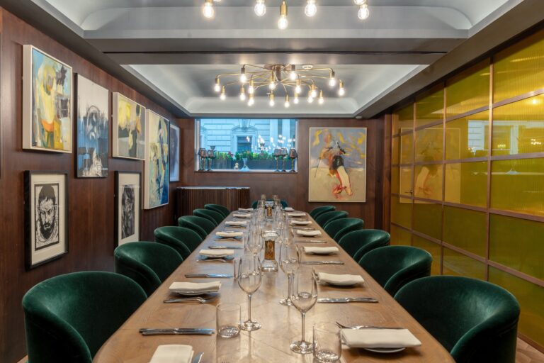 The Private Dining Room laid for a long dinner, with art on the walls and a view of Waterloo Place, Sofitel London St James