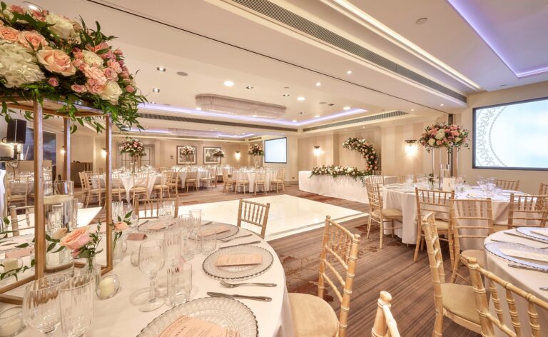Round tables with tall floral centrepieces around a dance floor, set for a wedding reception, Sofitel London St James