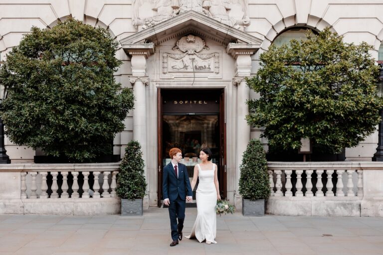 A bride and groom walking out of the carved stone entrance on Waterloo Place, Sofitel London St James
