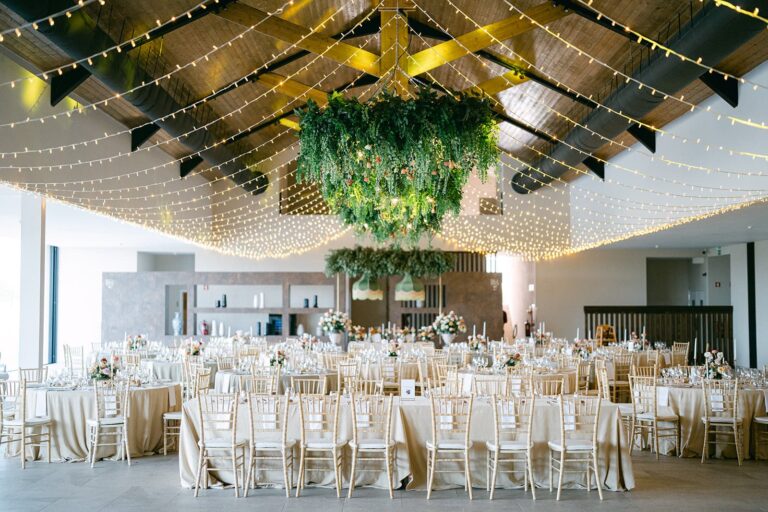 The Main Hall laid with round tables beneath strings of fairy lights and a hanging garland of greenery, Solar do Paço Algarve