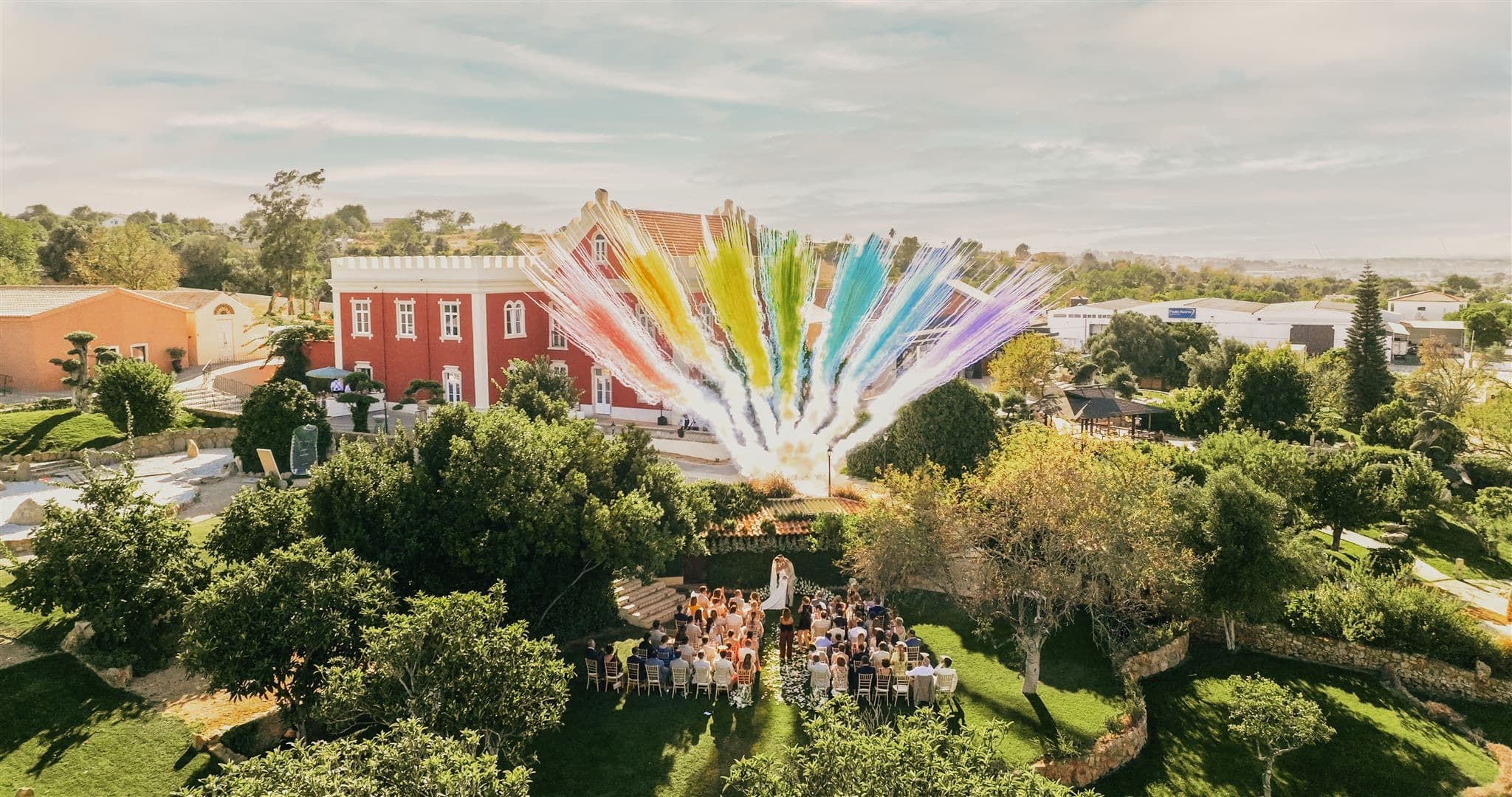 Aerial view of a garden ceremony with guests seated and coloured smoke rising beside the Palace, Solar do Paço Algarve