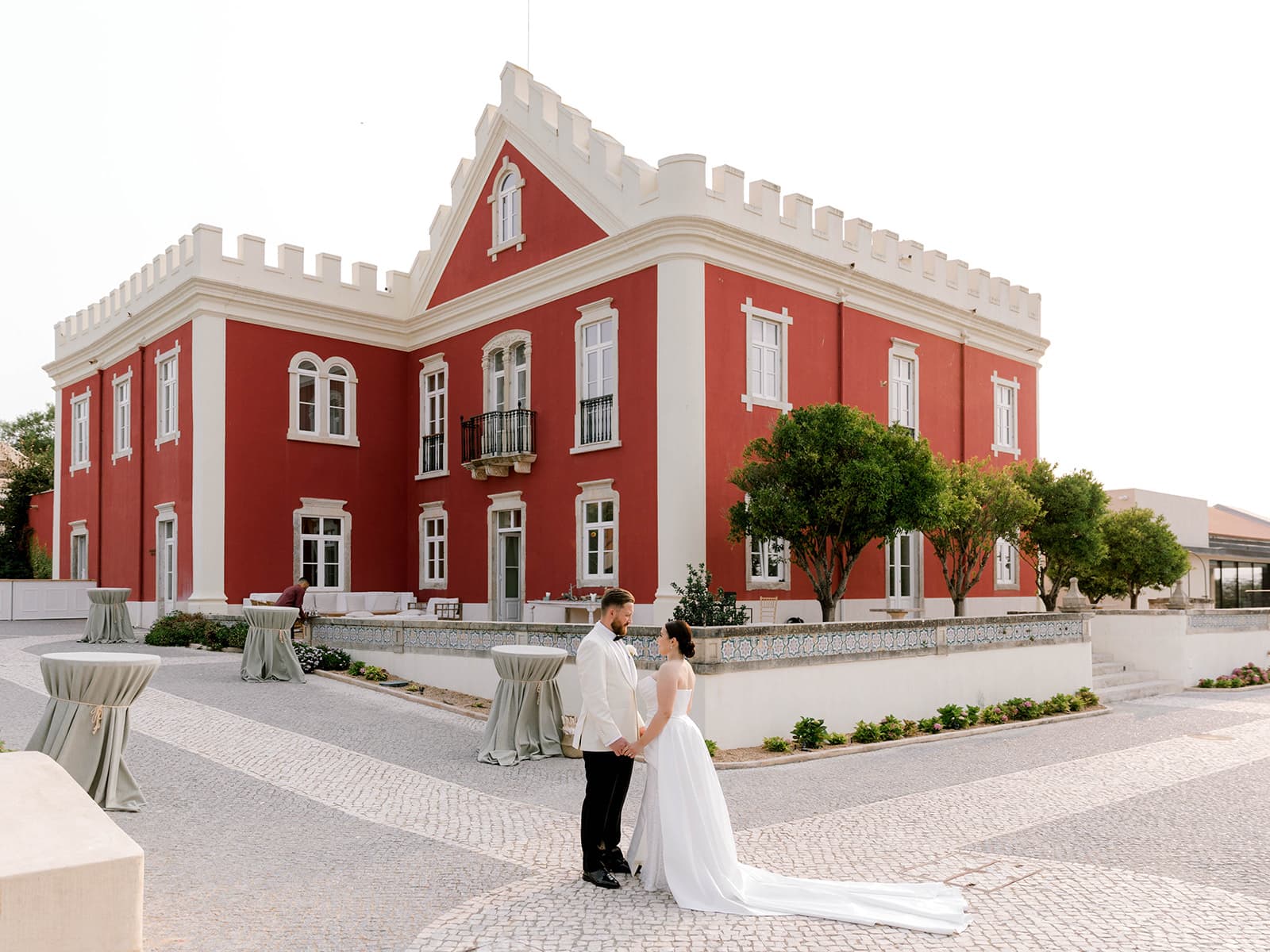 A couple standing on the cobbled terrace in front of the red Palace, Solar do Paço Algarve