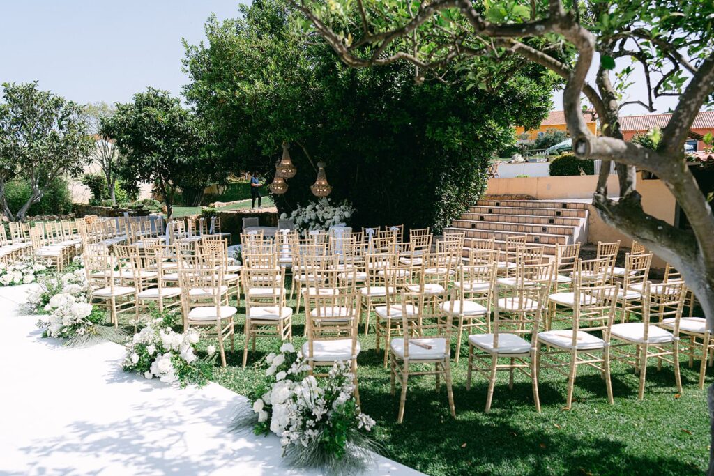 Rows of gold chairs on the grass beside a white aisle, with stone steps and trees, set for an outdoor ceremony, Solar do Paço Algarve