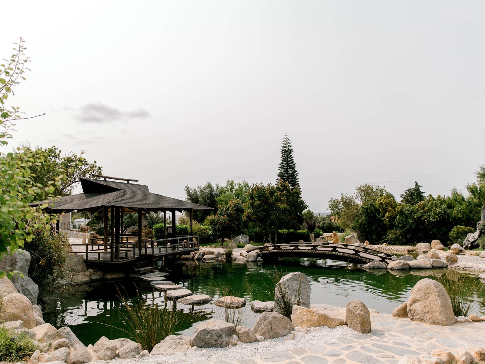 The Japanese garden pond with a wooden pavilion and an arched bridge among rocks, Solar do Paço Algarve