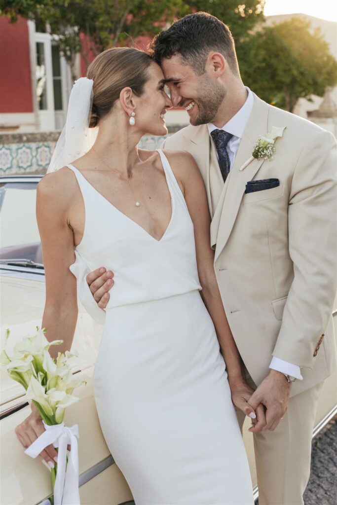 A couple holding hands beside a cream convertible, the bride holding white calla lilies, Solar do Paço Algarve
