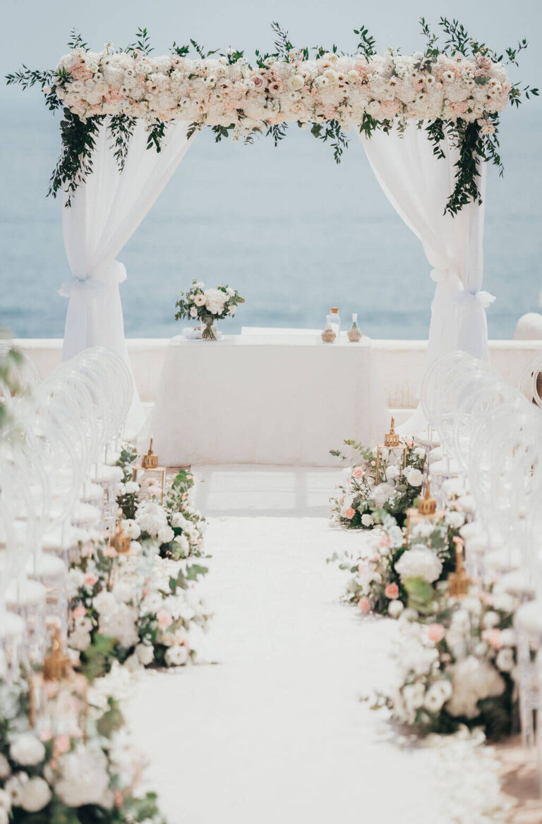 Flower-topped ceremony arch and aisle of white chairs beside the sea, Sonho a Dois Algarve Wedding Planners