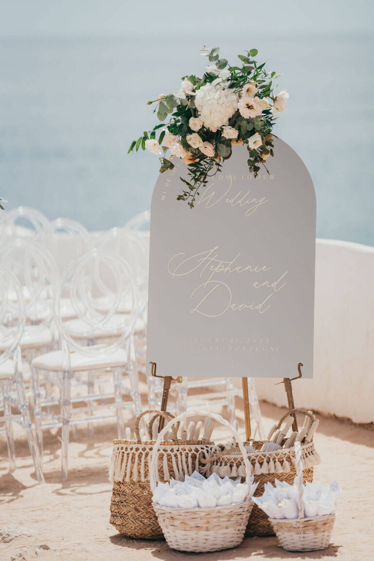 Welcome sign with a floral spray beside baskets of confetti, Sonho a Dois Algarve Wedding Planners