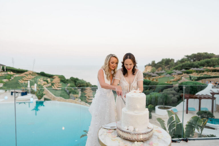 Two brides cutting their cake beside an infinity pool above the coast, Sonho a Dois Algarve Wedding Planners
