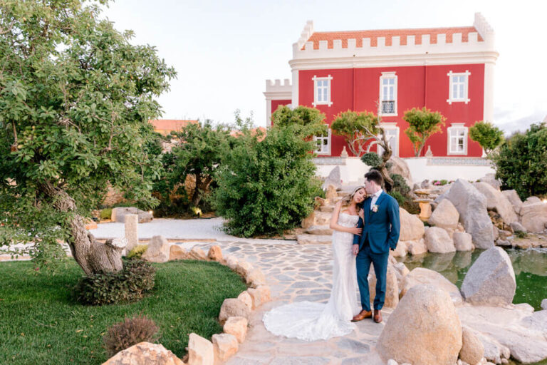 Bride and groom on the garden paths below a red-painted manor house, Sonho a Dois Algarve Wedding Planners