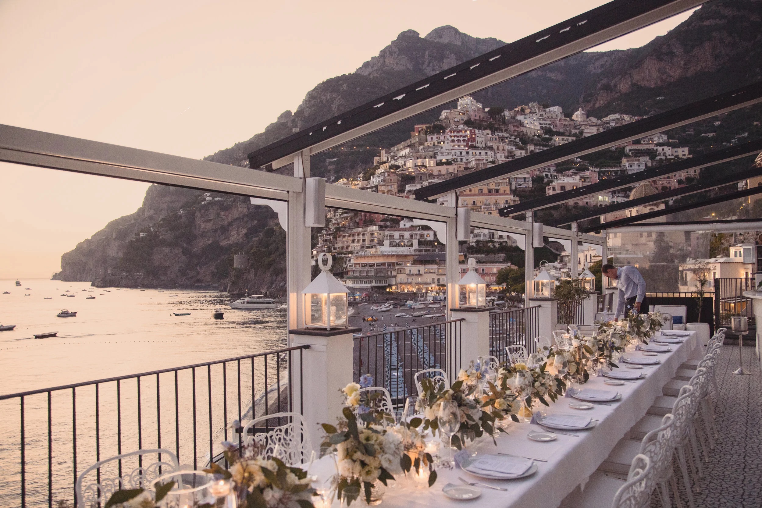 Long table dressed with white flowers and lanterns on the terrace at Rada, Positano, at dusk, Sophisticated Weddings