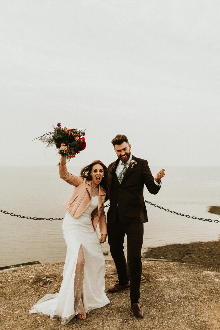 A couple celebrate on the clifftop, the coast behind them, Sorcha Herbert Flowers