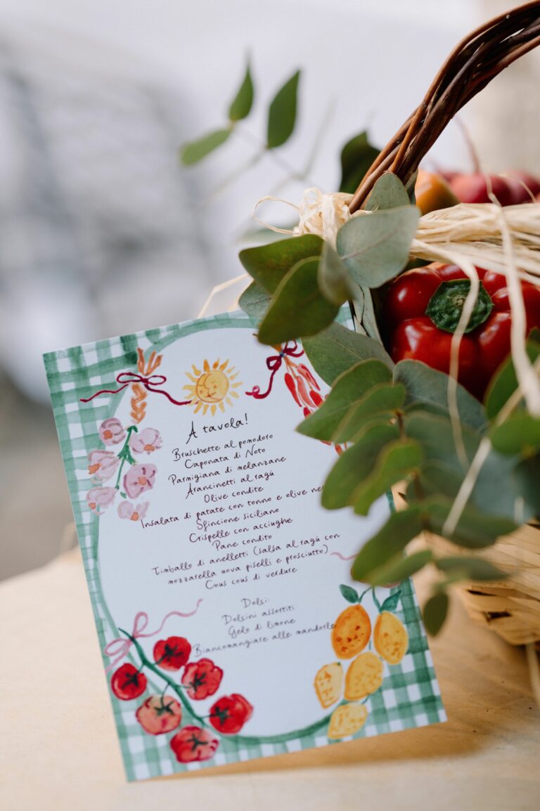 A hand-lettered "A tavola!" menu card tucked into a market basket of tomatoes, peppers and lemons, Sparx Wedding & Event Planner
