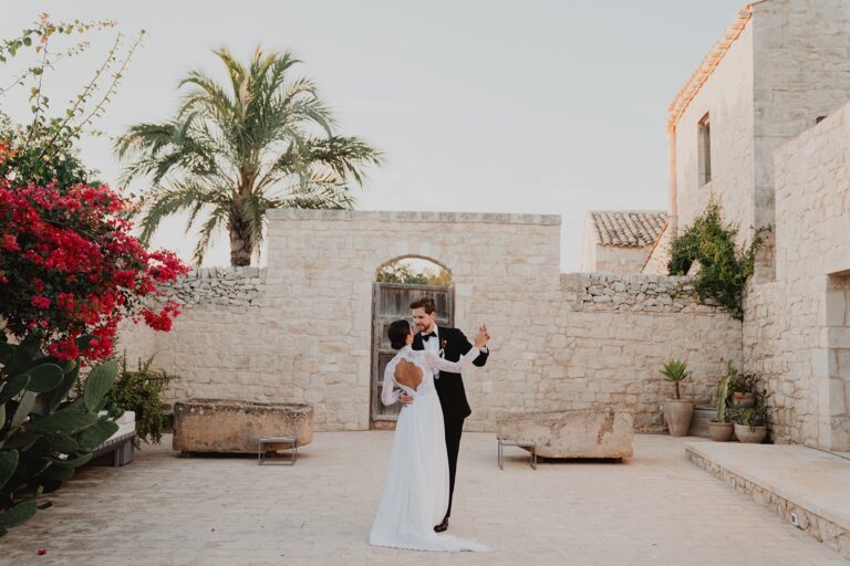 The couple's first dance at dusk in a walled Sicilian courtyard, bougainvillea spilling over the stone beside them, Sparx Wedding & Event Planner