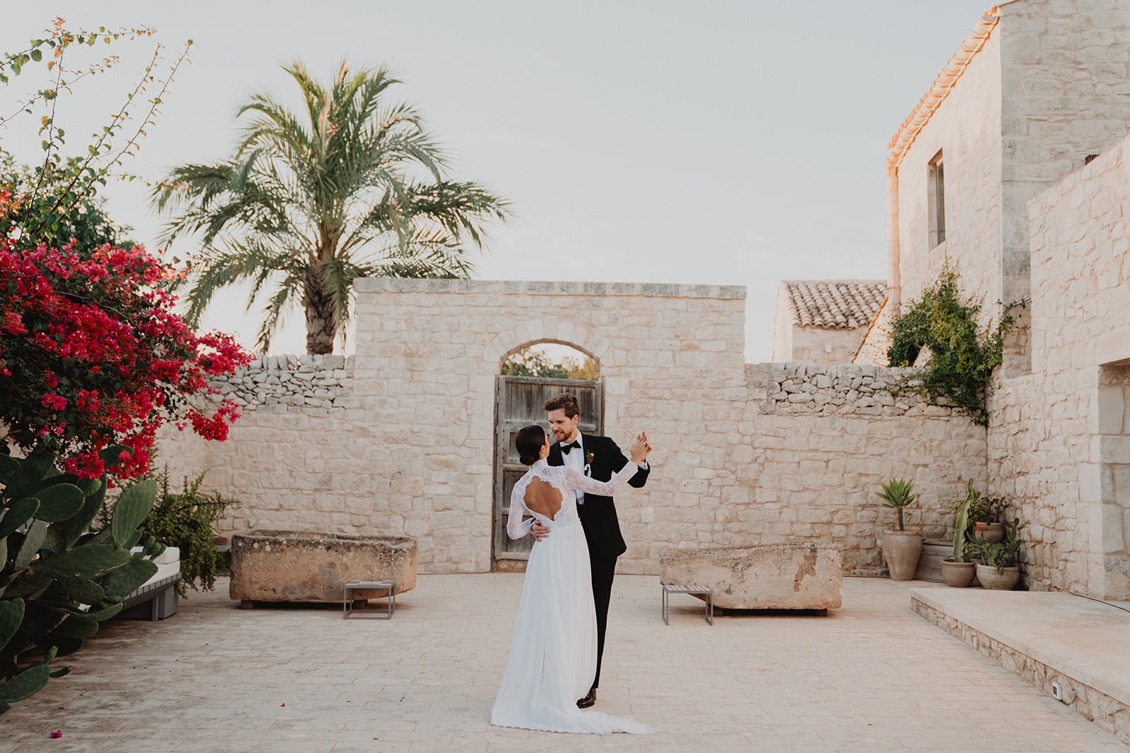 The couple's first dance at dusk in a walled Sicilian courtyard, bougainvillea spilling over the stone beside them, Sparx Wedding & Event Planner