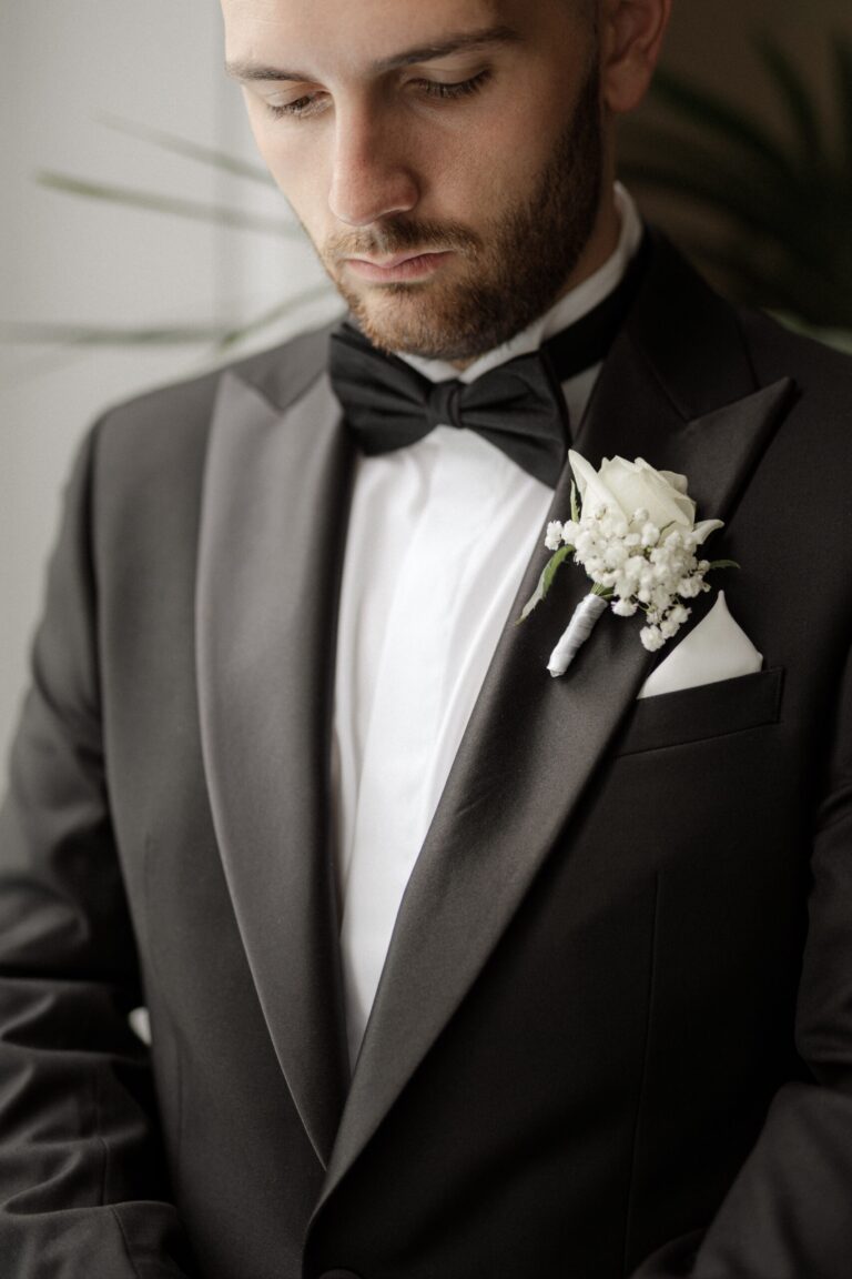 A close detail of the groom's boutonniere, a single white rose pinned to his black lapel, Sparx Wedding & Event Planner