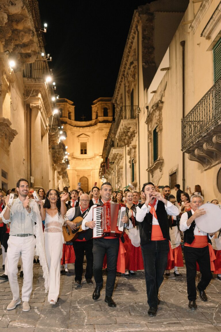 A traditional Sicilian folk band leads the couple through Noto's lit streets after dark, accordion and tambourine in hand, Sparx Wedding & Event Planner