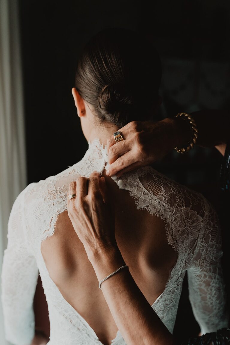The bride's lace gown fastened up the back, hands closing the final button, Sparx Wedding & Event Planner
