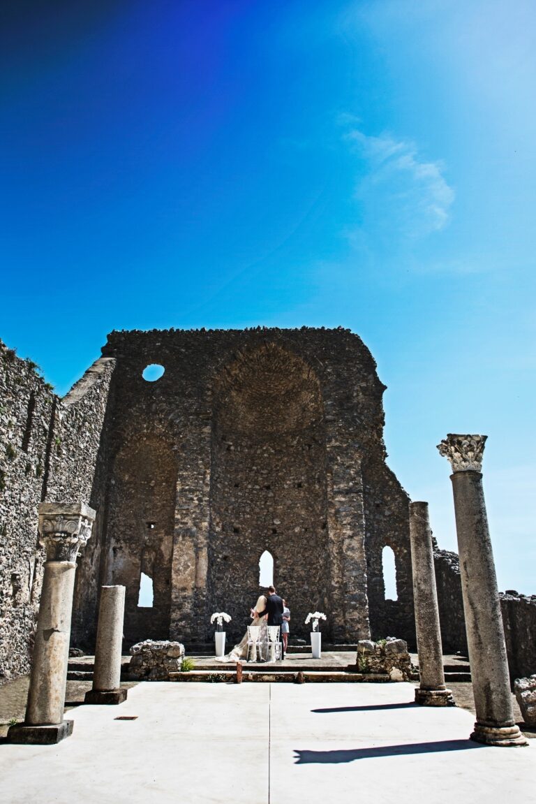 A ceremony inside a roofless basilica, the columns standing, the sky hard blue, Sposa Mediterranea By A&C