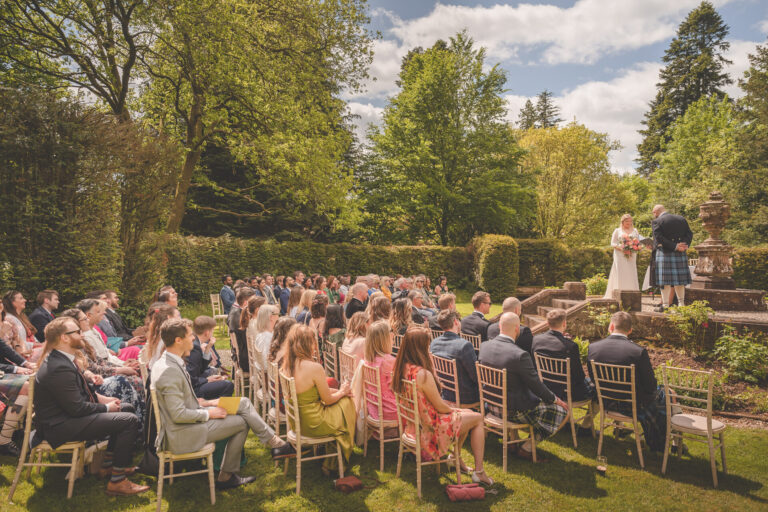 An outdoor ceremony in the Round Garden, with guests seated on the lawn and the couple by the stone urn, Springkell