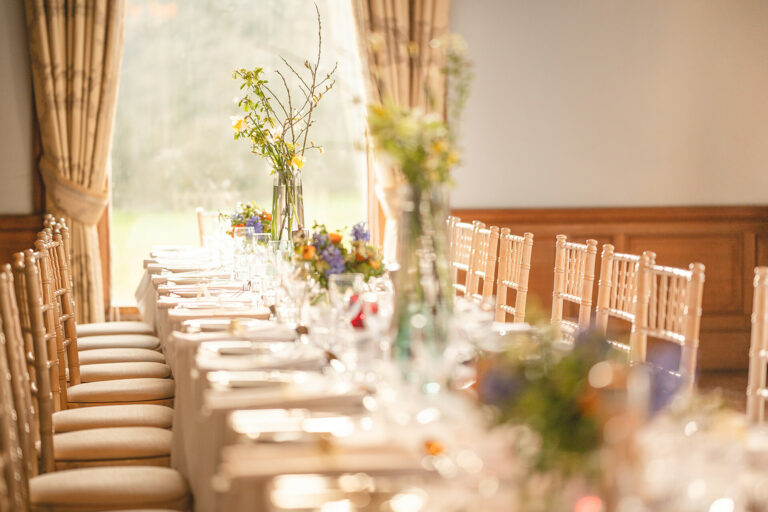 Wild-style flowers in glass vases along a table by a tall window, Springkell