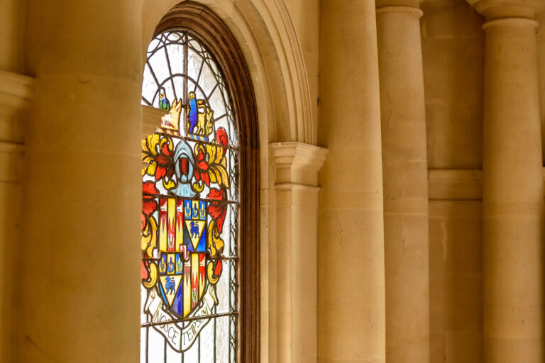 An armorial stained glass window set between stone columns in the porch, Springkell