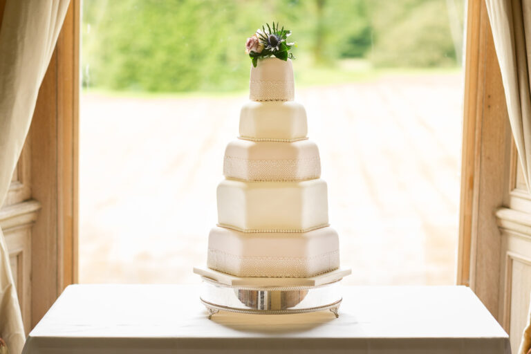 A five-tier white wedding cake on a silver stand in a window, Springkell