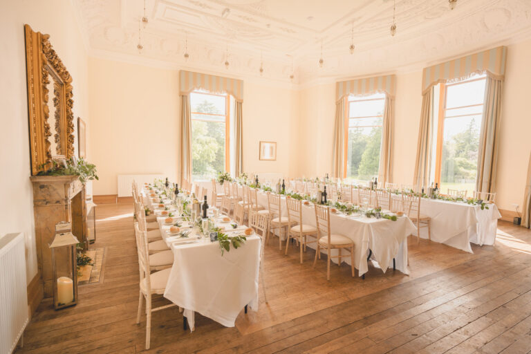 Long tables with greenery runners in a bow-windowed room with a gilt mirror over the fireplace, Springkell